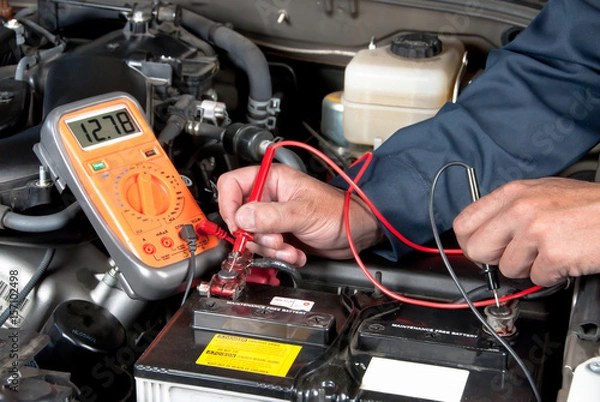 Fototapeta Auto mechanic checking car battery voltage