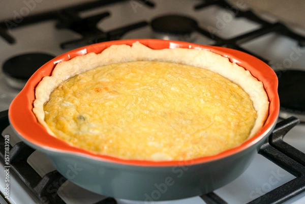 Fototapeta Freshly baked hot aromatic Quiche Lorraine with spinach and cheese on the stove in the kitchen. Close-up. Selective focus.