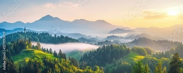 Obraz Sunrise over misty, forested hills with layered mountain ranges in the background, creating a serene and picturesque natural landscape.