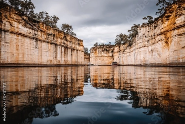 Fototapeta Calm river reflecting sandstone cliffs under a cloudy sky