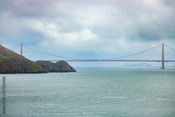 Fototapeta Close-up view of the Golden Gate Bridge rising behind rugged coastal cliffs of Marin Headlands, captured on a moody overcast day in San Francisco Bay, California