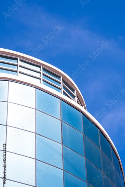 Fototapeta Modern curve geometric office building with blue sky reflection on glass wall surface, view from below and vertical frame