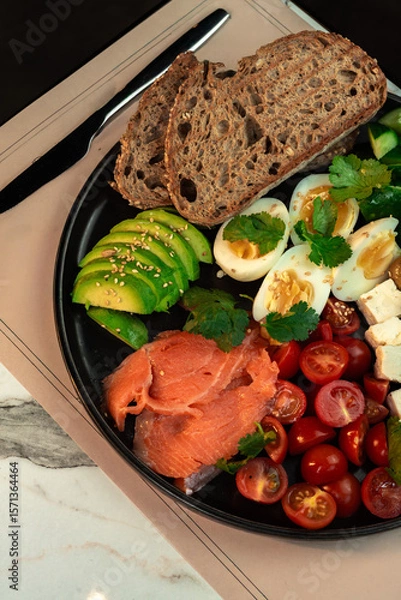 Fototapeta Hearty Smoked Salmon Breakfast Bowl with Avocado, Egg & Feta. Multigrain bread, cherry tomatoes, cucumber and olives plated for a nutritious morning meal.