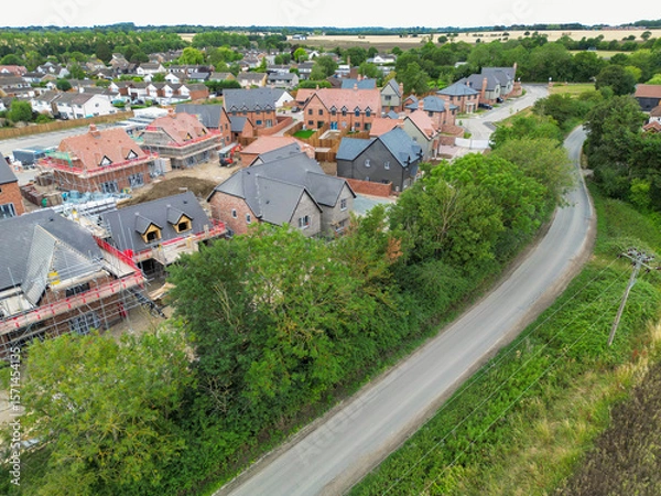 Fototapeta Aerial view of nearly completed, expensive and detached family homes seen on a housing development site in rural Essex, UK. A country lane snakes passed to the development to a nearby old village.