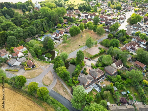 Fototapeta Picturesque drone view of a typical British rural village showing the village green surrounded by houses and a small pond.  Seen near a road junction leading to the village.