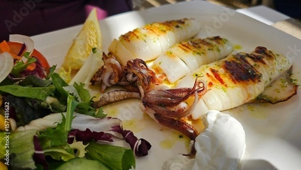 Fototapeta Grilled full squids calamari on the white plate with lemon and green salad leaves on the side 
