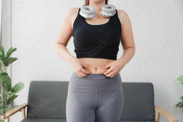 Fototapeta Body Shape Assessment: A close-up perspective showing a person pinching skin around belly, highlighting concerns about body shape and fat content.