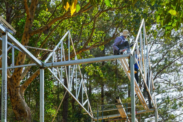 Fototapeta Welding Metal Frame in Nature, Workers Assembling Steel Structure Among Forest Trees