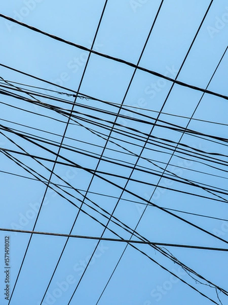 Fototapeta Tangled Power Lines Crisscross Against a Clear Blue Sky in a Chaotic Urban Overhead Utility Network