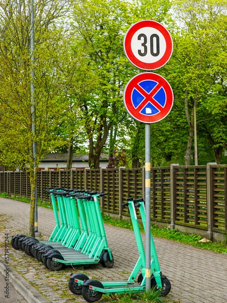 Fototapeta Electric Scooters Parked Near Speed Limit and No Parking Signs on Tree-Lined Urban Sidewalk
