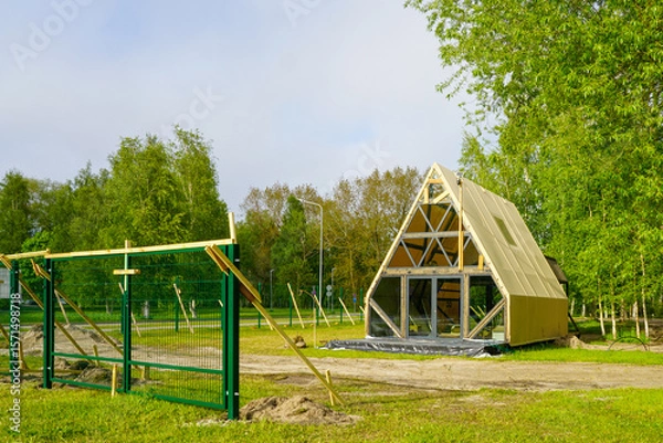 Fototapeta New A-Frame Glamping Cabin Under Construction in a Forested Campground with Green Fence Nearby