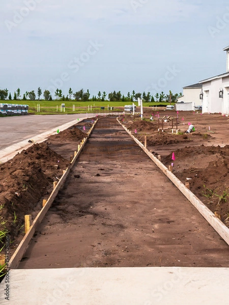 Obraz Perspective of future sidewalk, with wooden stakes and formwork in place for pouring of concrete to extend existing sidewalk, alongside a new street in a suburban residential development in Florida