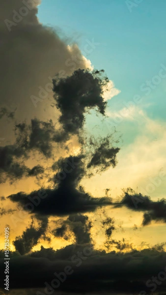 Obraz Ragged clouds in silhouette at golden hour in Florida, drifting so as to suggest the form of someone in a skirt walking across the evening sky. Motifs of perception, connections, anthropomorphism.