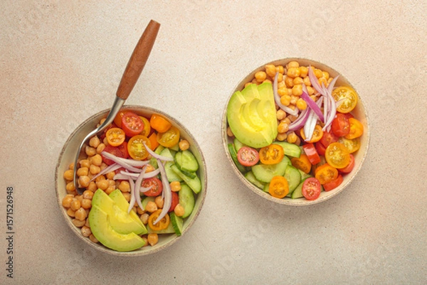 Obraz Two bowls of healthy chickpea salad with ripe avocado, juicy cherry tomatoes, crisp cucumber, and red onion slices. Perfect for a nutritious and healthy meal, light beige background