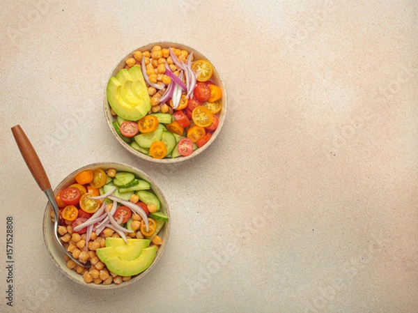 Obraz Two bowls of healthy chickpea salad with ripe avocado, juicy cherry tomatoes, crisp cucumber, and red onion slices. Perfect for a nutritious and healthy meal, light beige background, copy space