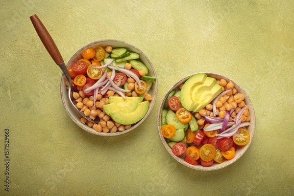 Obraz Two bowls of healthy chickpea salad with ripe avocado, juicy cherry tomatoes, crisp cucumber, and red onion slices. Perfect for a nutritious and healthy meal, light green background
