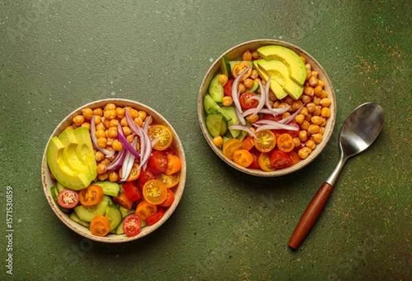 Obraz Two bowls of healthy chickpea salad with ripe avocado, juicy cherry tomatoes, crisp cucumber, and red onion slices. Perfect for a nutritious and healthy meal on green background