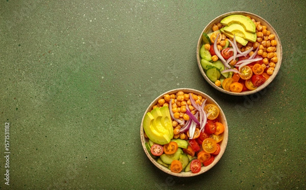 Obraz Two bowls of healthy chickpea salad with ripe avocado, juicy cherry tomatoes, crisp cucumber, and red onion slices. Perfect for a nutritious and healthy meal on green background, copy space