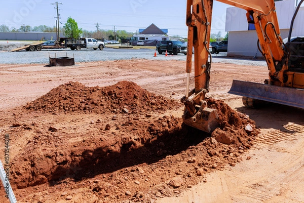 Fototapeta Excavator works on construction site creating trench while trucks are parked nearby during works area