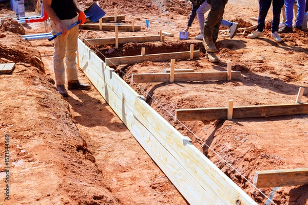 Fototapeta Workers are assembling wooden forms for foundation of new structure at construction site