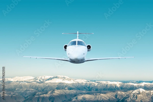 Obraz Front view of the white modern luxury executive aircraft flies over snow covered mountains