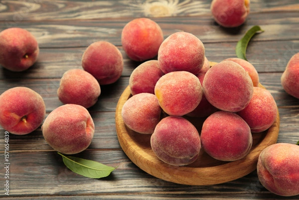 Obraz Sweet peaches and leaves on wooden plate on brown background. Space for text