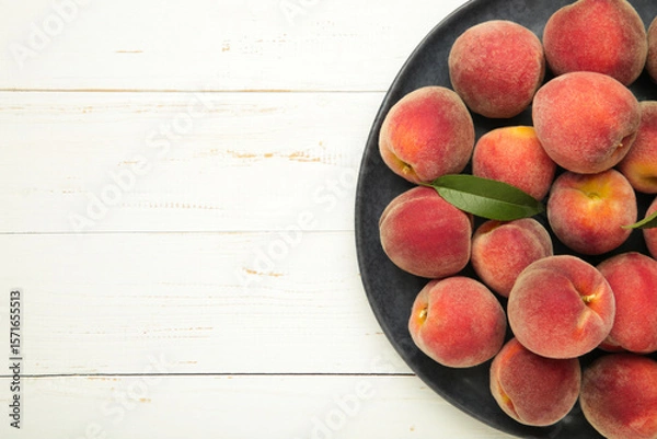Obraz Sweet peaches and leaves on dark plate on white wooden background. Space for text