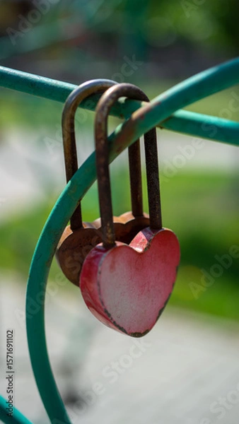 Fototapeta Padlock in shape of red heart hangs on fence. Symbol of eternal love and strong relationships. Vertical image