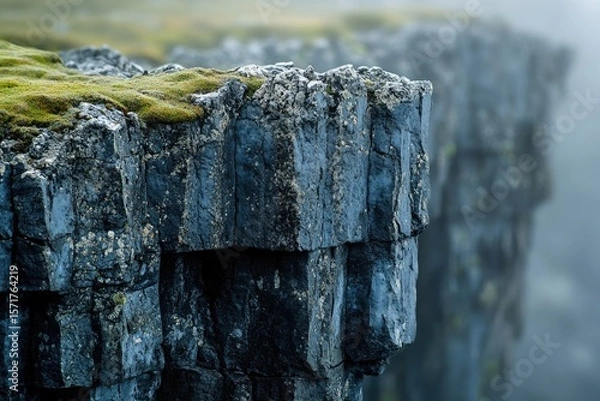 Fototapeta Rugged rock cliffs stand prominently, adorned with vibrant green moss, against a blurred background shrouded in atmospheric mist and soft, muted colors.