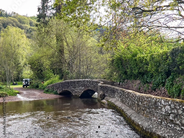 Fototapeta Dunster UK, March 15, 2025. The Gallox Bridge in Dunster, Somerset, England dates from the 15th century. with two arches over the River Avill. It was originally known as Gallows Bridge