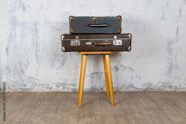 Fototapeta Two vintage suitcases stand on a stool against a white wall. The concept of retro travel and retro design.