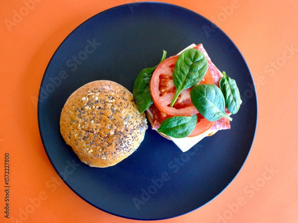 Obraz A cold Danish salami burger with cheese, tomato and spinach leaves on a brioche bun with seeds. 