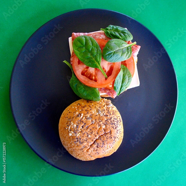 Obraz A cold Danish salami burger with cheese, tomato and spinach leaves on a brioche bun with seeds. 