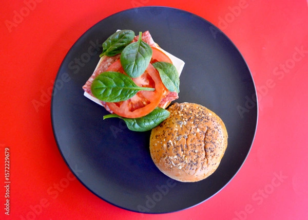 Obraz A cold Danish salami burger with cheese, tomato and spinach leaves on a brioche bun with seeds. 