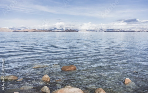 Fototapeta Rocky shore of Lake Karakul and blue water of a high mountain lake against the background of rocky mountain slopes in the Pamirs in the Tien Shan, panoramic landscape for background