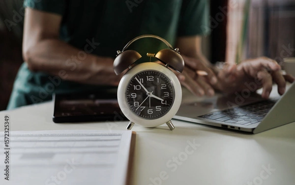 Fototapeta select focus on alarm clock, freelancer using laptop working in a hurry before deadline, time management concept, routine work, office hour