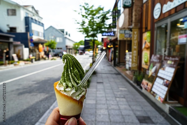 Fototapeta Enjoying milk ice cream soft serve cone with green tea flake powder on street footpath on sunny day