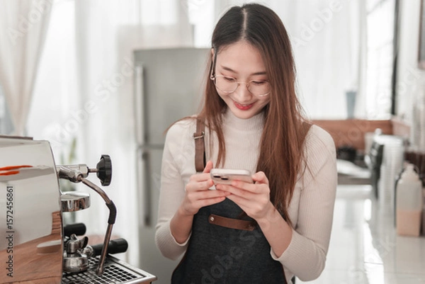 Obraz Young woman enjoys coffee while engaging with smartphone in cozy coffee shop atmosphere