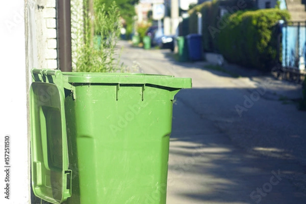 Fototapeta Green garbage container with the lid open on empty residential street in small European town. Concept of waste disposal, environmental issues, city cleanliness and municipal waste management services