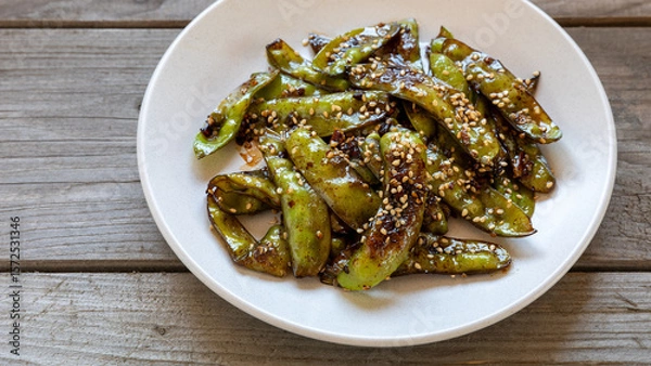 Fototapeta Asian Sugar Snap Peas dish. Pea pods stir-fried with garlic, ginger, and soy sauce, and sprinkled with toasted sesame seeds. Rustic table.