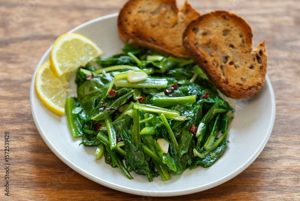 Obraz Sauteed Chicory Greens - a traditional Italian side dish on a plate served with toasted bread and slices of lemon.
