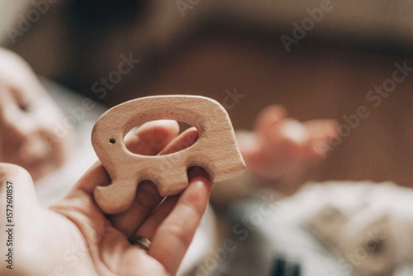 Obraz Infant extends hand toward a wooden elephant toy held nearby. The handcrafted toy captures the baby's attention, representing a moment of curiosity and early learning.