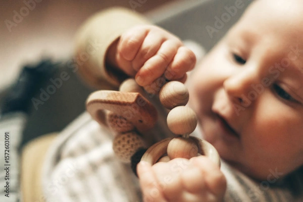 Obraz Close-up of a baby gnawing on a wooden teething toy, showcasing their curiosity and oral exploration. The image captures the baby's focus and engaging hand movements.