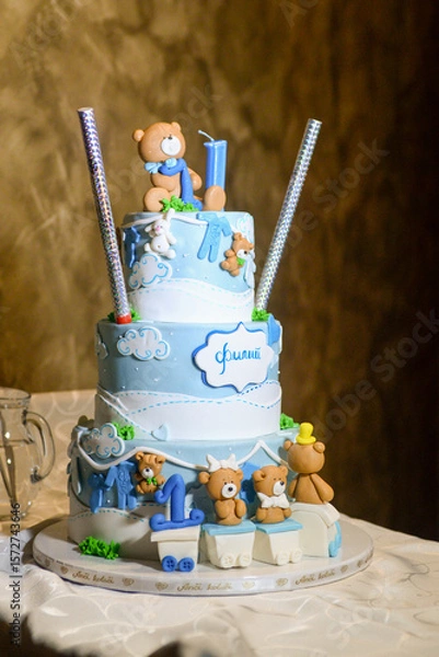 Fototapeta A three-tier blue and white birthday cake decorated with fondant, figurines in the shape of bears and a bunny with the male name Philip written in Cyrillic.