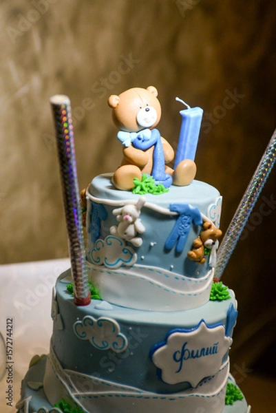 Fototapeta A three-tier blue and white birthday cake decorated with fondant, figurines in the shape of bears and a bunny with the male name Philip written in Cyrillic.
