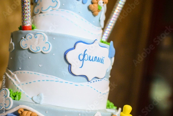 Fototapeta A three-tier blue and white birthday cake decorated with fondant, figurines in the shape of bears and a bunny with the male name Philip written in Cyrillic.