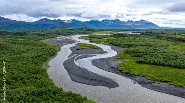 Fototapeta Breathtaking panoramic view of South Iceland's dramatic landscape featu a meande river flowing through lush green vegetation and majestic snow-capped mountains under a