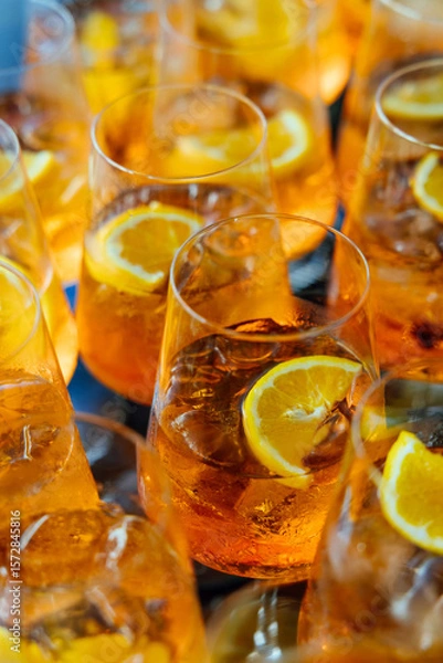Fototapeta Close-up of multiple Aperol Spritz cocktails garnished with fresh orange slices, creating a vibrant and festive party atmosphere.
