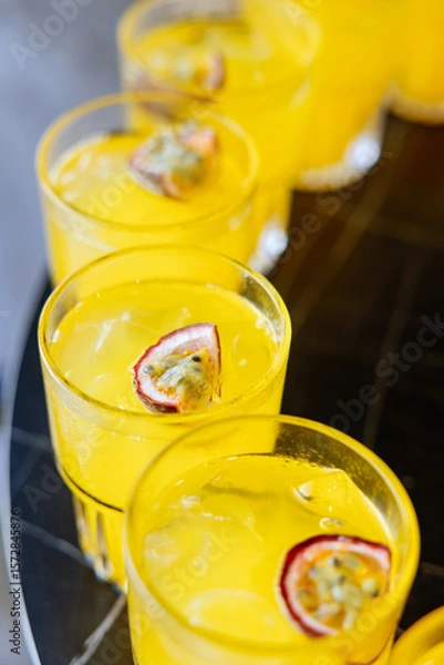 Fototapeta Close-up of vibrant yellow cocktails with passion fruit garnish, served on a tray at a party or summer event.
