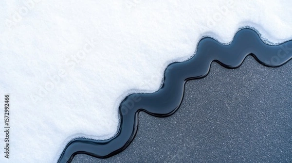 Fototapeta Close-up of black liquid spilling on white snow forming wavy border pattern on asphalt surface